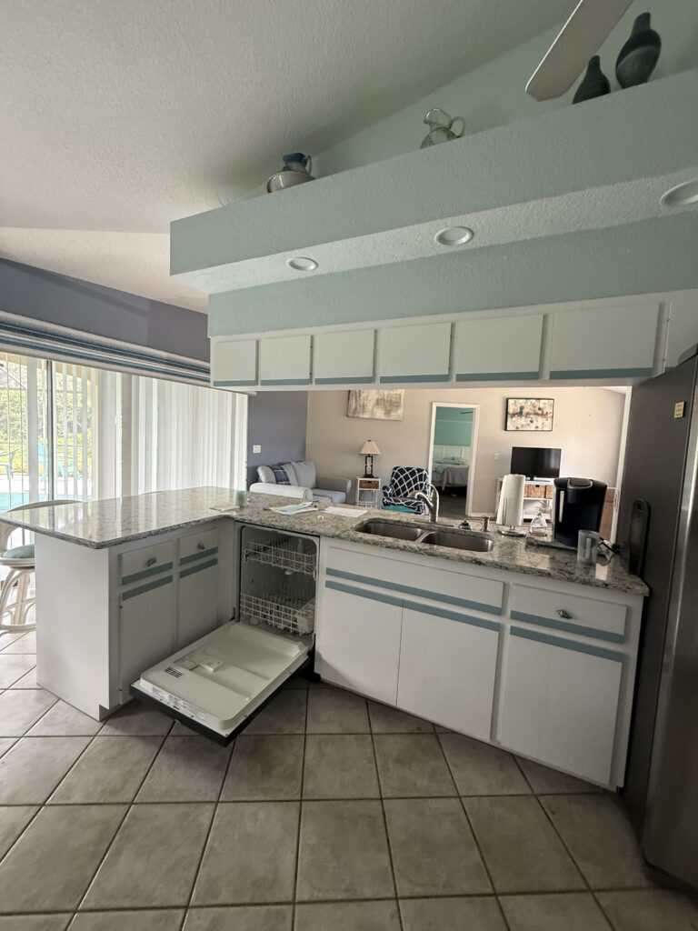 Dated kitchen with white cabinets and granite counters opening to the living room